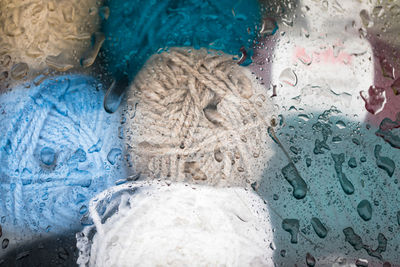 Close-up of colorful yarn balls seen through wet glass window