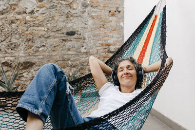 Portrait of smiling woman lying on hammock against wall