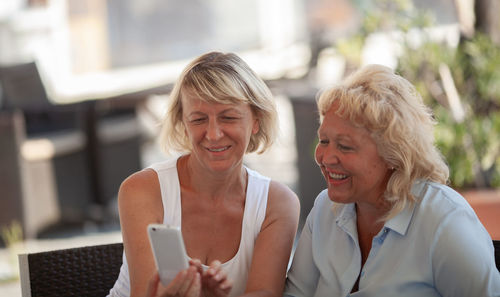 Happy friends looking at mobile phone in cafe