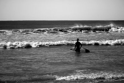 Silhouette man walking with surfboard at sea