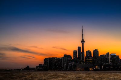 River against cn tower amidst buildings in city at sunset