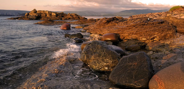 Rocks in sea against sky during sunset