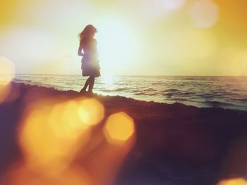 Silhouette woman standing at beach during sunset