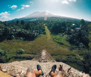 Low section of young man sitting on mountain against sky