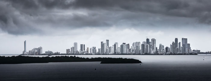 City at waterfront against cloudy sky