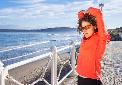 Young woman standing by railing against sea