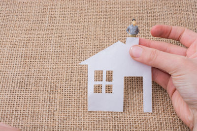 Cropped hand holding paper model home with male figurine at table