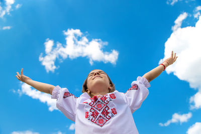 Low angle view of girl with arms raised against sky