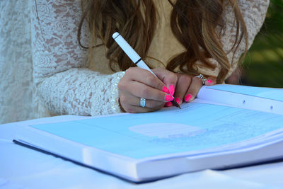 Midsection of bride writing in book on table