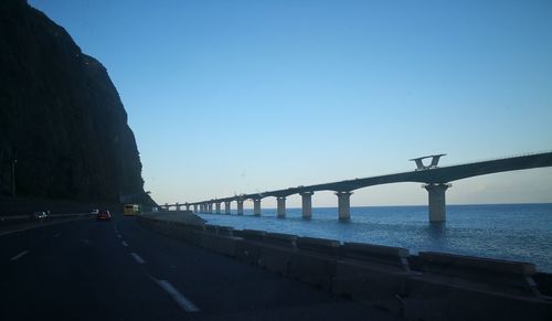 Bridge over calm sea against clear blue sky