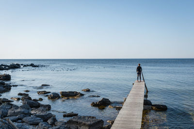 Rear view of man standing on rocks by sea against sky