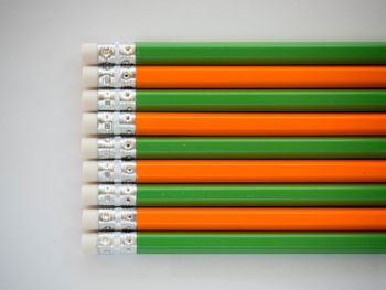 Directly above view of green and orange pencils on white table