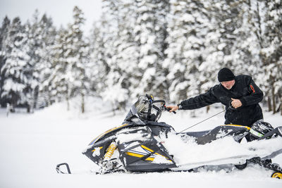 Senior man starting snowmobile with pull cord.