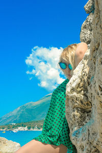 Portrait of woman standing by rock against blue sky