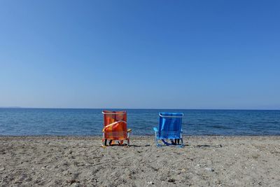 Rear view of deck chairs on beach against clear blue sky