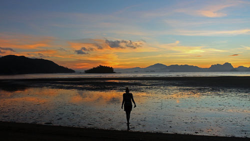 Silhouette woman walking on beach against sky during sunset