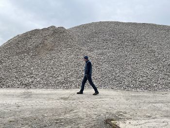 Rear view of man walking on land or rocks against sky