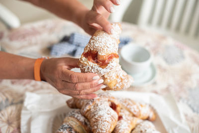 Tasty brioche filled with jam, split by feminine hands during breakfast