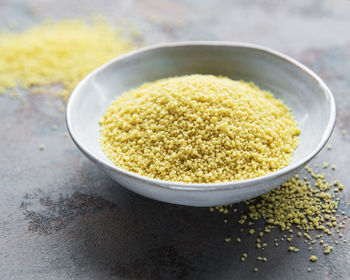 Raw couscous in a white bowl on the grey concrete background