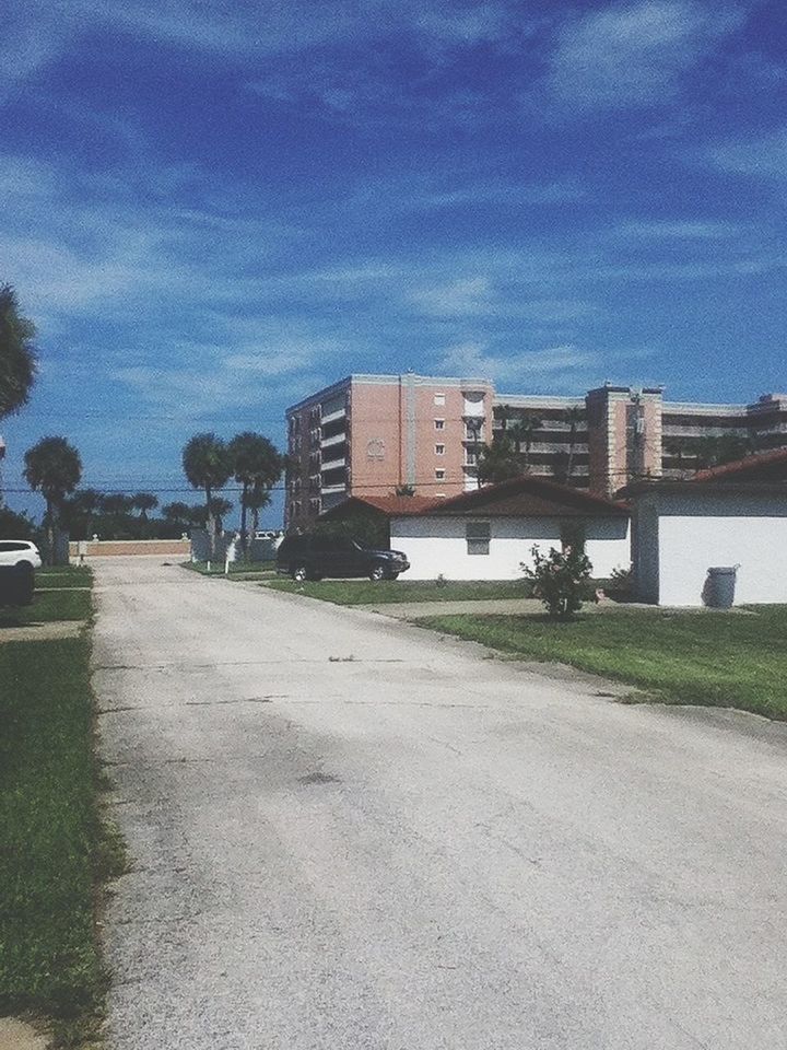 building exterior, architecture, built structure, the way forward, sky, road, street, transportation, diminishing perspective, empty, vanishing point, cloud - sky, city, tree, road marking, cloud, walkway, footpath, grass, day