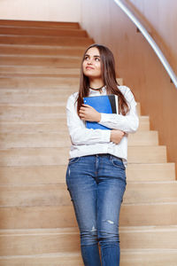 Young woman holding book while standing on steps