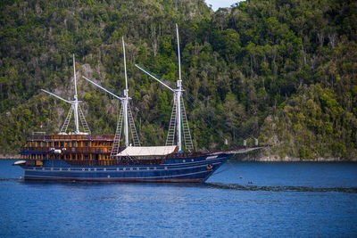 Ship sailing in blue sea against rocky mountains