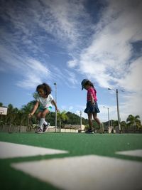 Friends playing on grassy field at park against sky