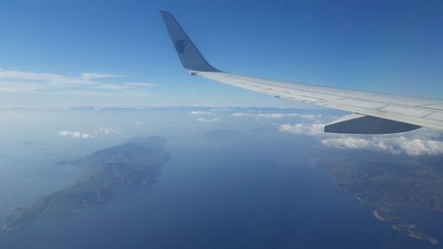 Aerial view of airplane wing over landscape against blue sky