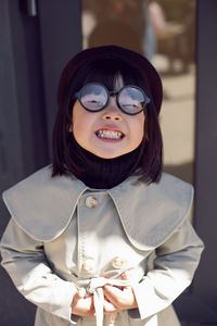 Korean girl in a gray coat and cap and round glasses stands the street in spring at the glass doors