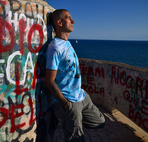Side view of young man standing against wall at sea