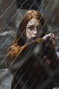 Portrait of young woman seen through chainlink fence