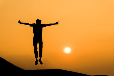 Silhouette man with arms raised against orange sky