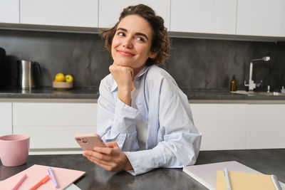 Portrait of young woman using mobile phone while sitting in office