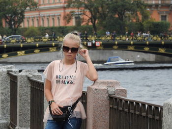 Portrait of girl wearing sunglasses while standing against canal in city