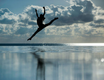 Full length of woman doing ballet dancing in infinity pool by sea against sky