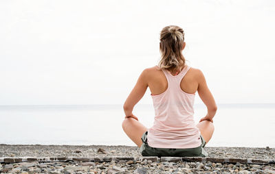 Full length rear view of woman sitting on beach against sea