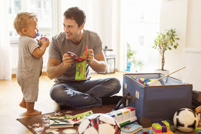 Smiling father showing toy to baby boy at home