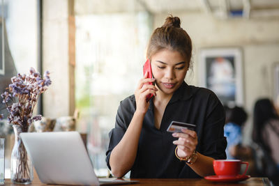 Woman talking on mobile phone while sitting at table in restaurant