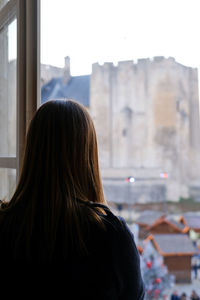 Rear view of woman standing by window against clear sky