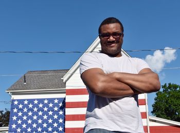 Portrait of man standing against american flag patterned house
