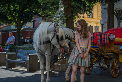 Young woman standing next to horse carriage on the street
