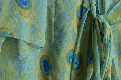 Detail of dress in fabric with peacocks plumage inspiration pattern