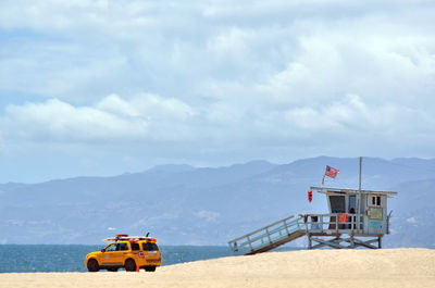 Off-road vehicle and lifeguard hut at beach against sky