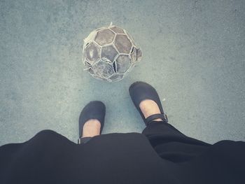 Low section of woman standing by old soccer ball on street