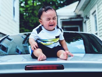 Full length of baby boy crying while sitting on car