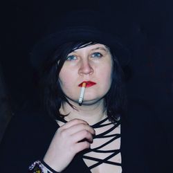 Close-up portrait of young woman smoking cigarette in darkroom