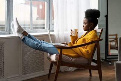 Young woman using laptop while drinking coffee at home