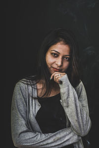 Portrait of young woman smoking against black background