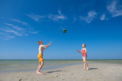 Full length of people playing on beach against blue sky