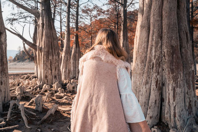 Rear view of woman standing by tree trunk in forest